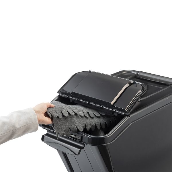 Probox Slanted 58L premium storage box made of black, post-consumer material. The container is in use, the man puts the blanket inside through a small hinged lid on the front.