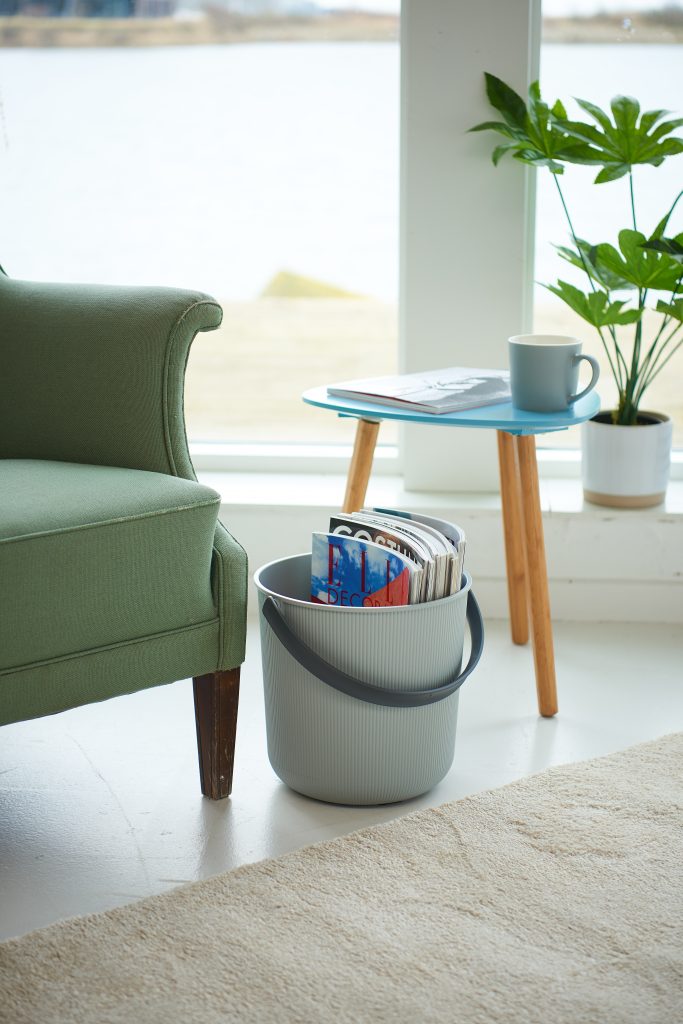 Akita storage buckets available in two sizes are great to store books or journals inside. A bucket is in a living room near the armchair and table.
